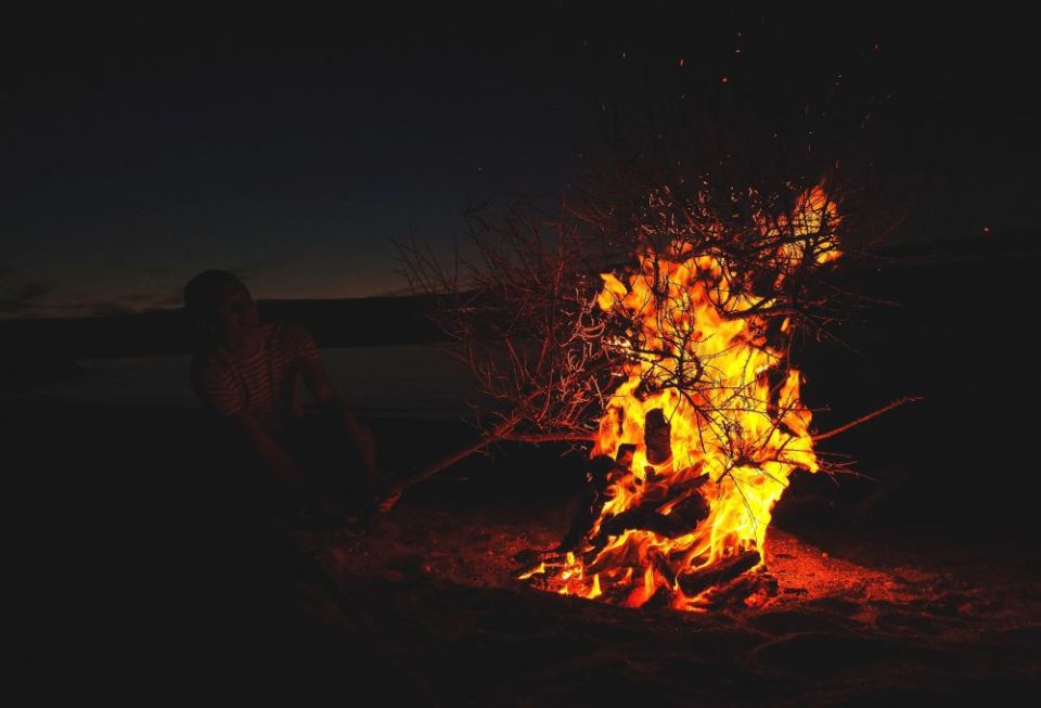 A person near a bonfire on a beach before sunrise in Courtown, Ireland (Unsplash/Traolách Conboy)