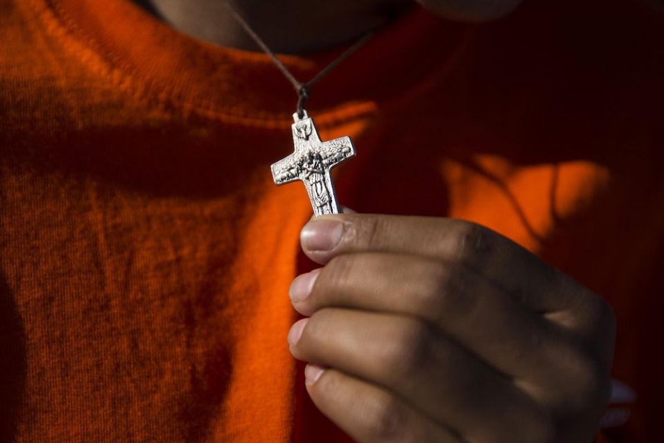 A young man holds a crucifix as he and other immigrants attend Mass on the U.S. side of the border in El Paso, Texas, Feb. 17, 2016. (CNS/Nancy Wiechec)