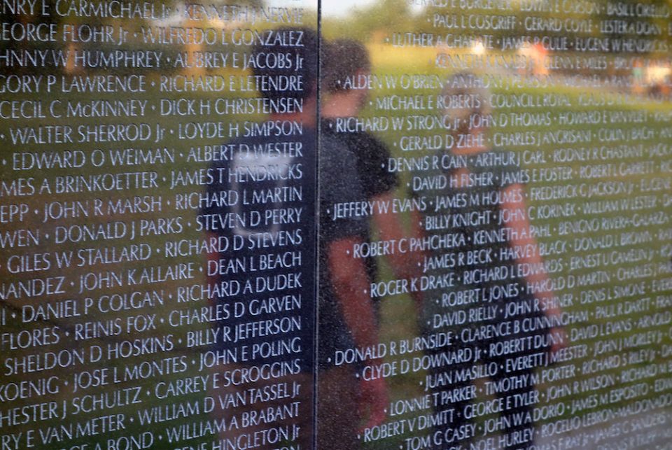 Black granite slabs of Maya Lin's "Vietnam Veterans Memorial" showing inscribed names and reflections of visitors walking