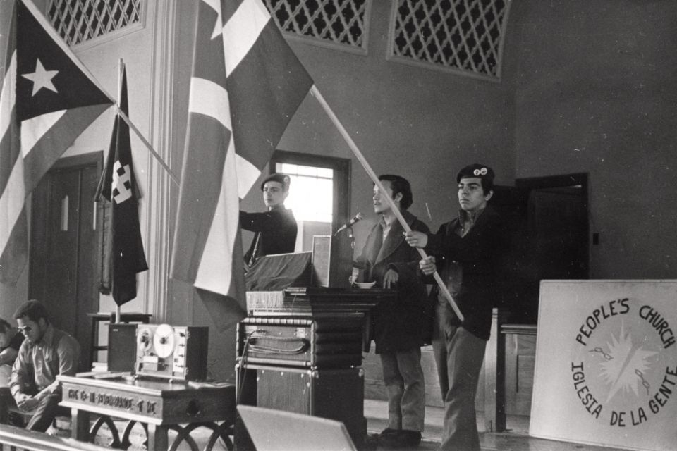 Young Lords members hold flags inside the Armitage Methodist Church in March 1970, commemorating the Masacre de Ponce. (Photo © Carlos Flores)