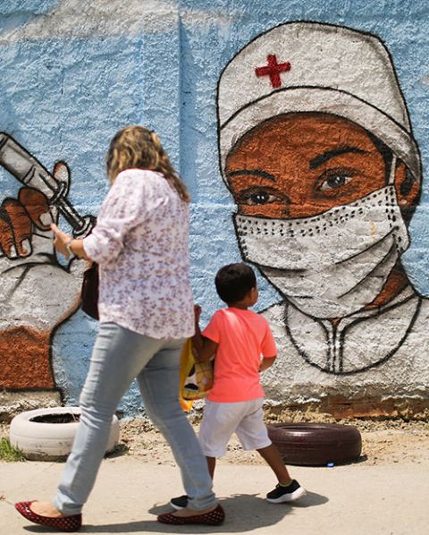 A woman and child walk past a painting on a wall in Rio de Janeiro March 12 during the COVID-19 pandemic. (CNS/Reuters/Pilar Olivares)