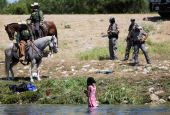U.S. law enforcement officers in Del Rio, Texas, stand near a young migrant woman bathing in the Rio Grande Sept. 19. (CNS/Reuters/Daniel Becerril)