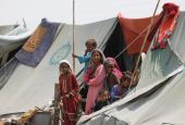 Children displaced by flooding stand outside their family tent while waiting for food handouts and relief material in Sehwan, Pakistan
