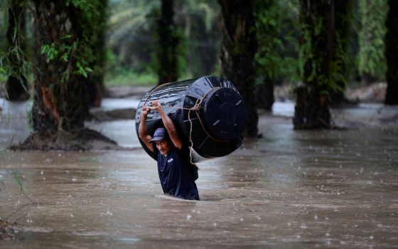 A man carries an empty water tank through a flooded area after the impact of tropical storm Julia in Progreso, Honduras, Oct. 9, 2022. (CNS photo/Yoseph Amaya, Reuters)